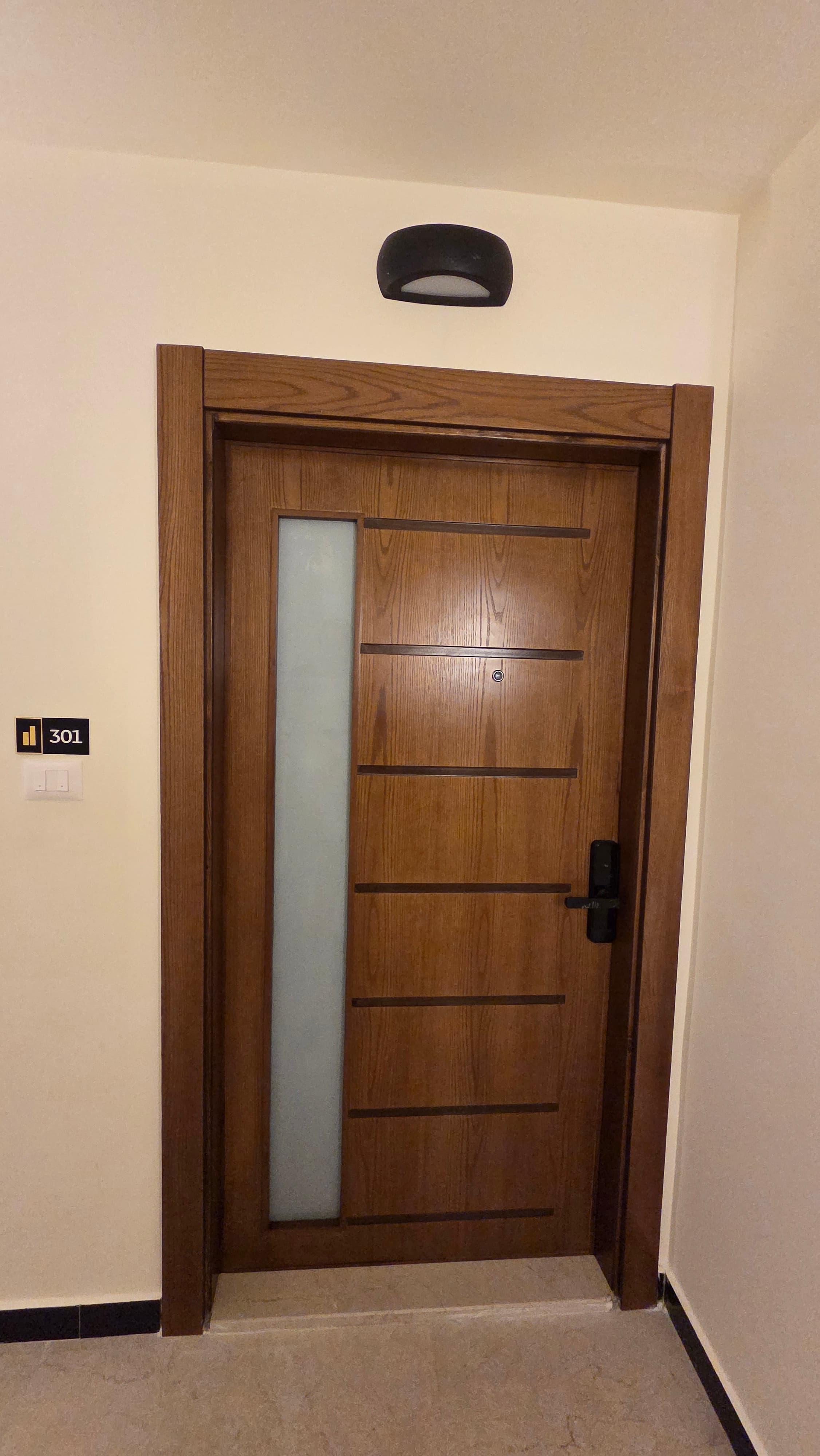 Walnut entrance door of Residence 301 with frosted glass panel, smart lock, and branded gold 301 plaque